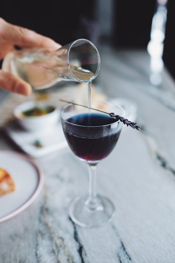 Lavender cocktail being delicately poured into an elegant glass, perfect for a sophisticated drink setup.
