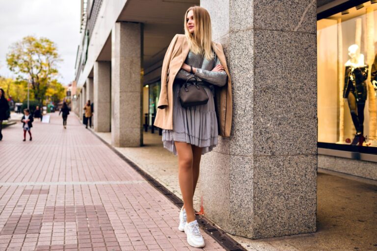outdoor lifestyle fashion portrait pretty elegant glamour blonde woman with long legs wearing trendy sneakers dress sweater coat posing europe city traveling alone 1.jpg